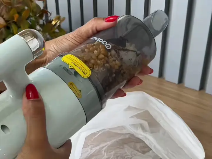 Reservatório do aspirador cheio de sujeira sendo esvaziado no lixo